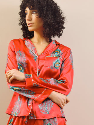 model wears long leg satin pyjamas in red with a peacock print. Detail