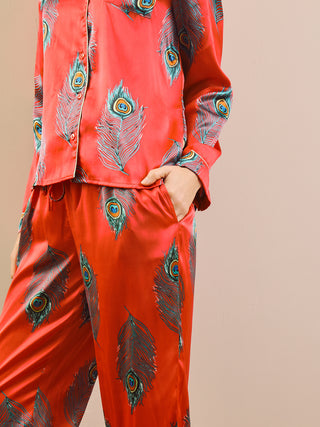 model wears long leg satin pyjamas in red with a peacock print. Pocket detail.