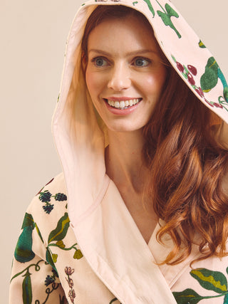 model wears a hooded velvet dressing gown with floral pair print on a cream base. 