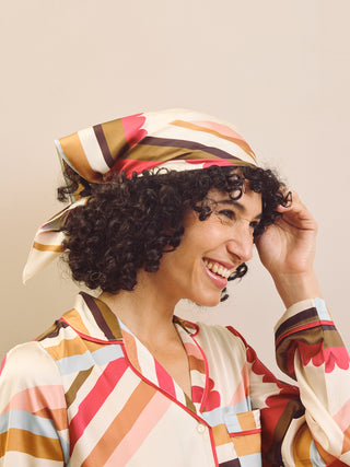 Woman wearing a colorful patterned headscarf and outfit against a beige background