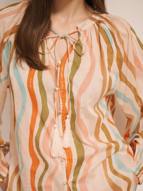Model wearing women’s cotton voile short pyjama set in oatmeal with rainbow wave print, featuring long-sleeve raglan top with tie neckline and matching short pyjama bottoms.