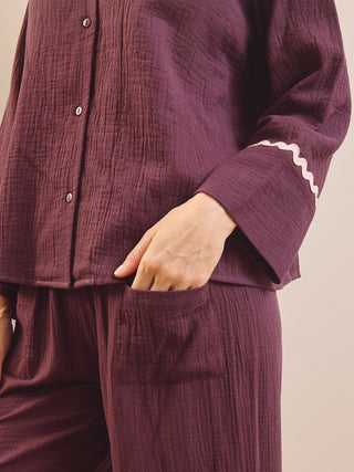 A close-up of a person wearing a matching mauve-purple crinkle gauze pyjama set with a button-front top and pants, featuring a white zigzag trim on the sleeve cuff.
