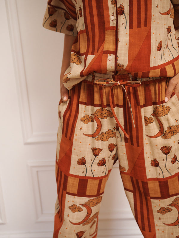 Model wearing women’s oversized linen blend pyjamas with natural patchwork sky flower print, featuring short-sleeve button-front shirt and wide-leg trousers in warm rust and neutral tones.