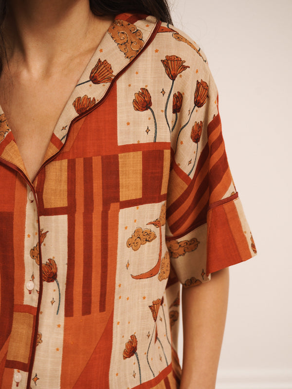 Model wearing women’s oversized linen blend pyjamas with natural patchwork sky flower print, featuring short-sleeve button-front shirt and wide-leg trousers in warm rust and neutral tones.