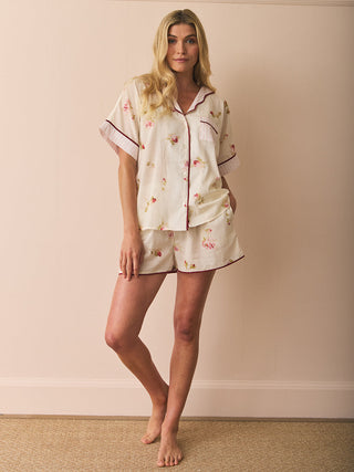 Woman wearing a sort floral pyjama set against a plain wall.