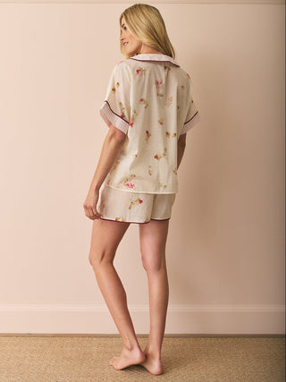 Woman wearing a short floral pyjama set against a beige wall.