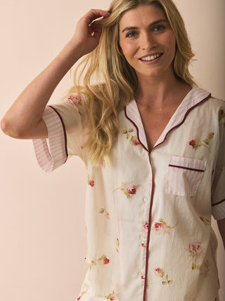 Model wears a floral and stipe pyjama set against a beige background