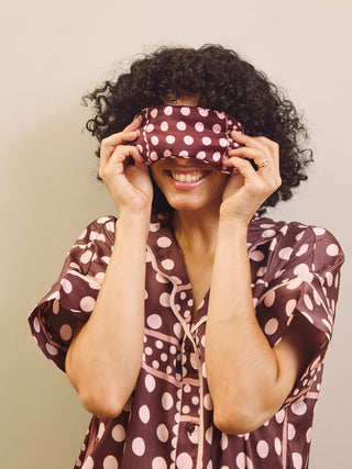 Person wearing a polka dot pyjama set holding a matching eye mask in front of their face.