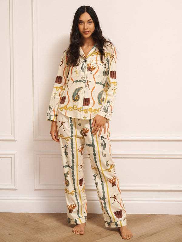 Model wearing women’s cotton traditional pyjama set in natural with sea life tile print, featuring long-sleeve button-front shirt with revere collar and matching straight-leg trousers with drawstring waist.