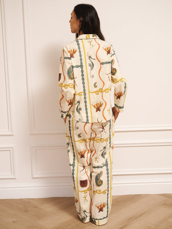 Model wearing women’s cotton traditional pyjama set in natural with sea life tile print, featuring long-sleeve button-front shirt with revere collar and matching straight-leg trousers with drawstring waist. Back detail