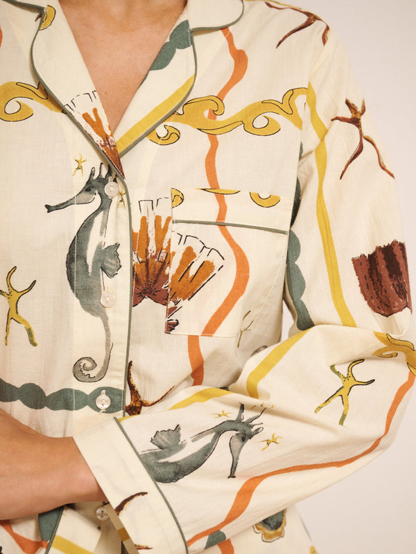 Model wearing women’s cotton traditional pyjama set in natural with sea life tile print, featuring long-sleeve button-front shirt with revere collar and matching straight-leg trousers with drawstring waist. Close up