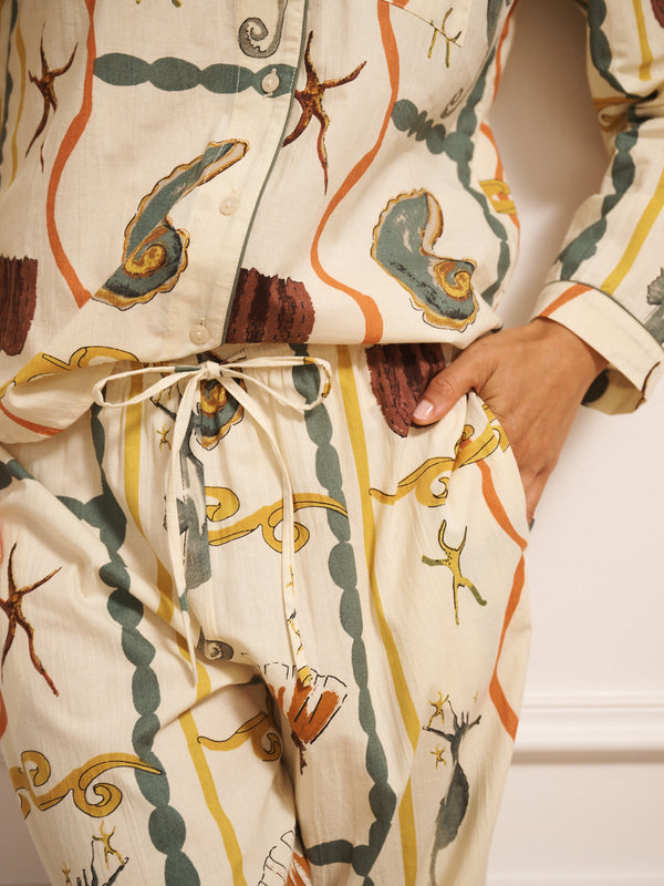 Model wearing women’s cotton traditional pyjama set in natural with sea life tile print, featuring long-sleeve button-front shirt with revere collar and matching straight-leg trousers with drawstring waist.
