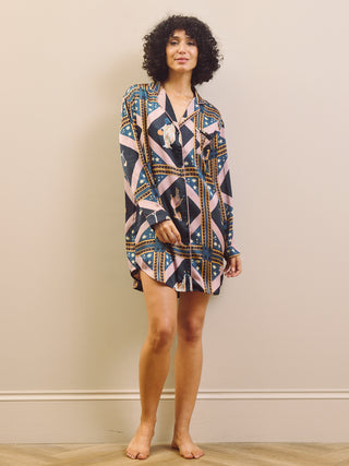 Woman wearing a patterned night dress standing against a plain wall.