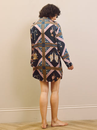 Woman wearing a patterned nightdress standing against a plain wall.