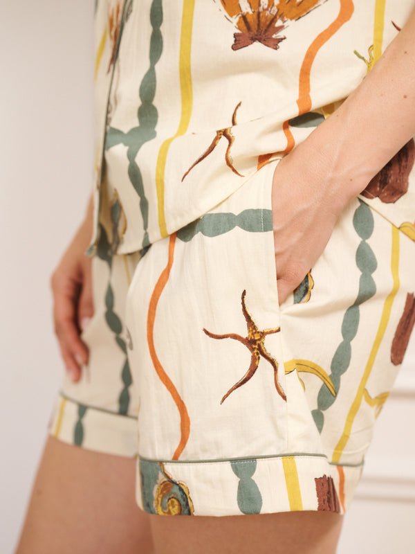 Model wearing women’s cotton shortie pyjamas in natural Sea Life Tile print, featuring a short-sleeved button-through top and matching shorts. Pocket detail. 