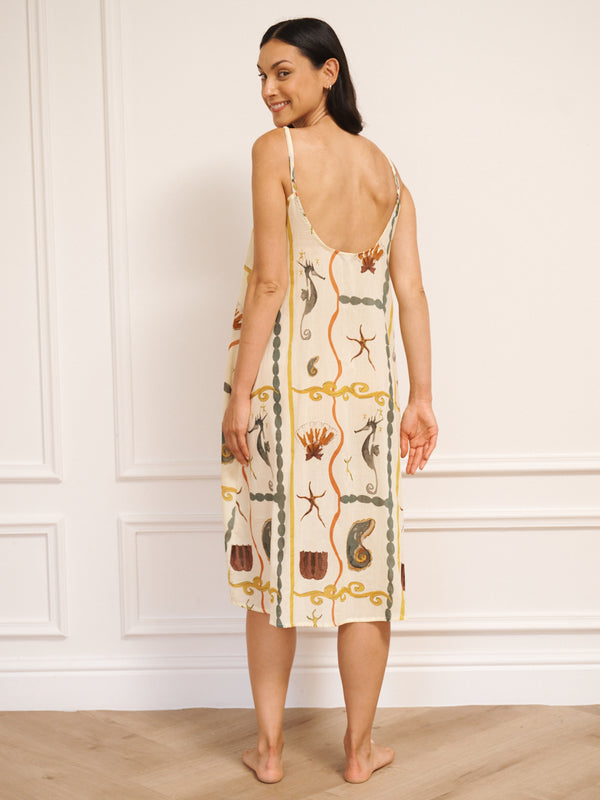 Model wearing women’s cotton voile midi nightdress with straight neckline and slim straps, featuring natural sea life tile print with seahorses, shells and starfish in a relaxed, flowing fit. Back detail.