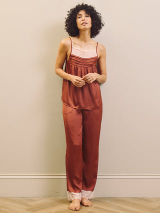 Woman wearing a rust-coloured pyjama set with lace trim against a beige wall.