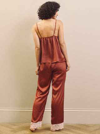 Woman wearing a rust-coloured satin pyjama set with lace trim against a beige wall.