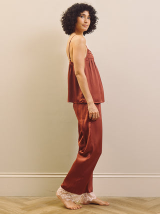 Woman wearing a rust-colored satin pyjama set with lace trim against a beige wall.