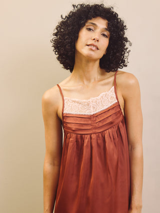 Woman wearing a rust-coloured pyjama cami top with lace details against a beige background