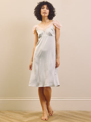 Woman wearing a light blue slip nightdress with lace trim against a beige wall.