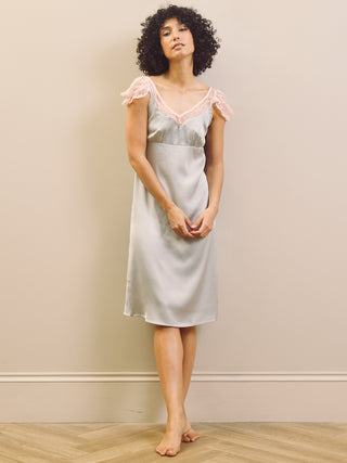 Woman wearing a light blue slip nightdress with lace trim against a beige wall.