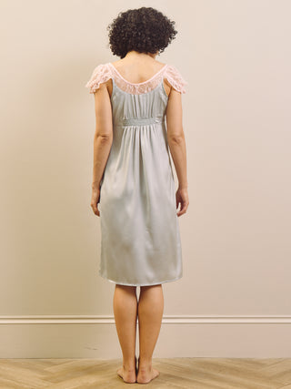 Woman wearing a light blue slip nightdress with lace trim against a beige wall.