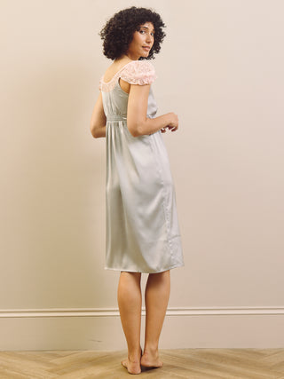 Woman wearing a light blue slip nightdress with lace trim against a beige wall.