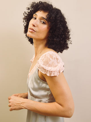 Woman wearing a light blue slip nightdress with lace trim against a beige wall.