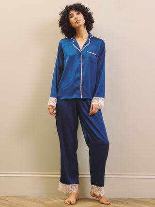 Woman wearing a blue satin pajama set with lace trim against a plain background