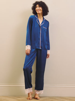 Woman wearing a blue satin pajama set with lace trim against a beige wall.