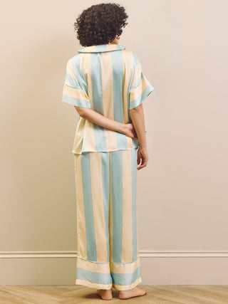 Person wearing a striped pyjama set with pastel colors against a beige wall.