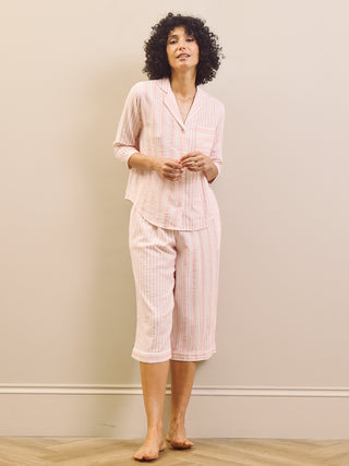 Woman wearing a pink striped pyjama set against a plain wall.
