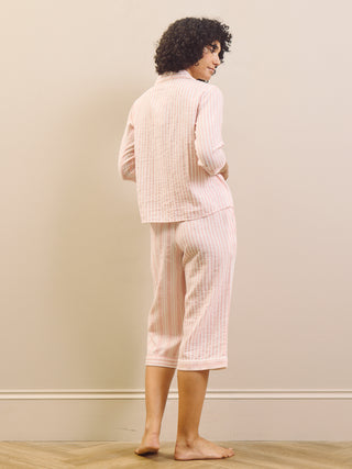 Woman wearing a pink striped pyjama set against a plain wall.