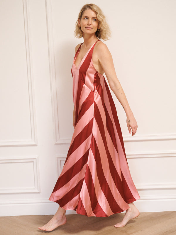 Woman wearing a red and pink striped night dress against a white wall.