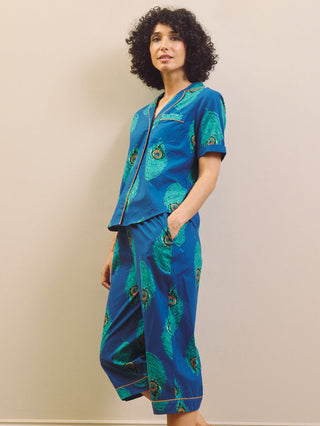 Woman wearing a blue peacock patterned capri pyjama against a beige wall.