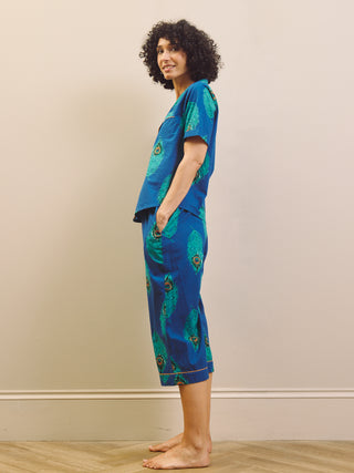 Woman wearing a blue peacock patterned capri pyjama against a beige wall.
