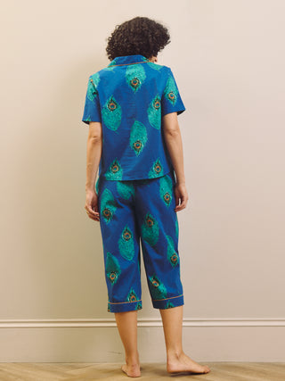 Woman wearing a blue peacock patterned capri pyjama against a beige wall.