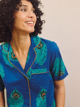 Woman wearing a blue peacock patterned capri pyjama against a beige wall.