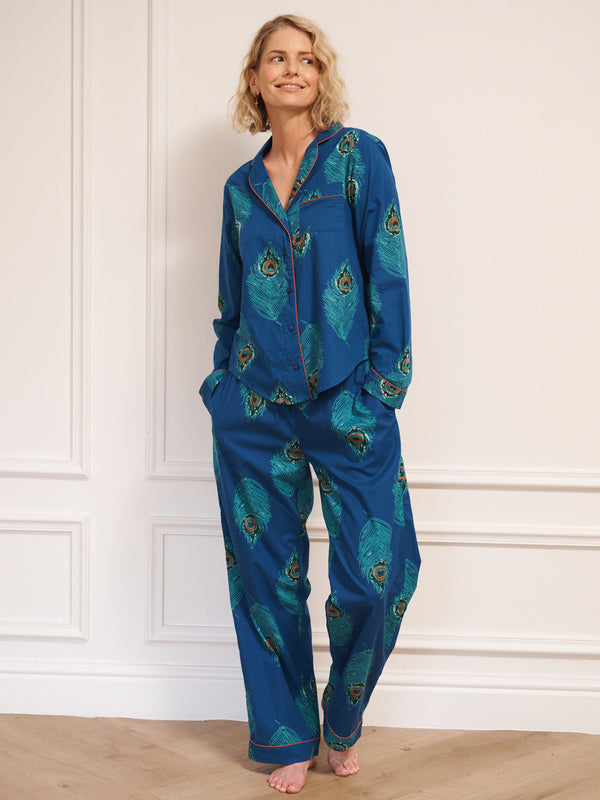 Woman wearing a blue pyjama set with peacock patterns against a white wall.