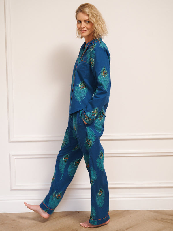 Woman wearing a blue pyjama set with peacock patterns against a white wall.