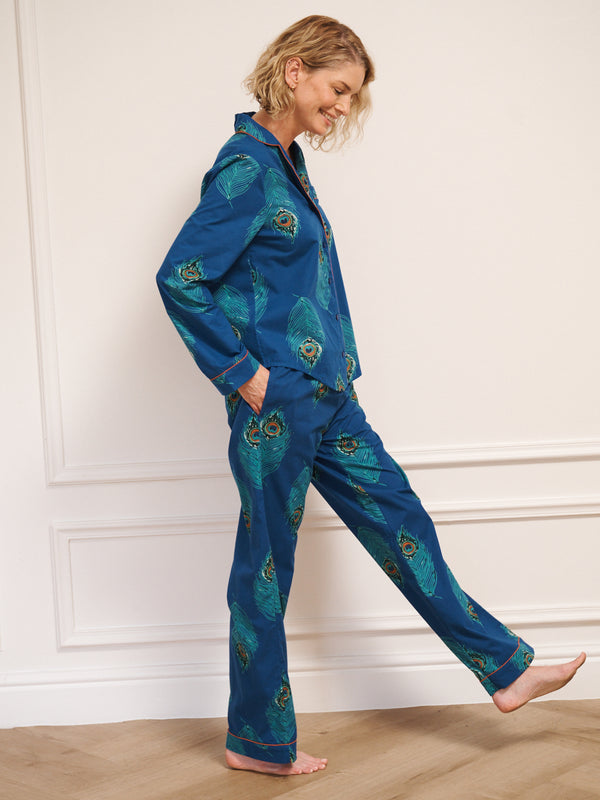 Woman wearing a blue pyjama set with peacock patterns against a white wall.