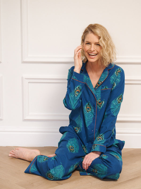 Woman wearing blue pyjamas with peacock patterns sitting on a wooden floor.