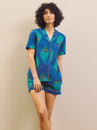Woman wearing a blue peacock patterned shirt pyjama set against a beige wall.