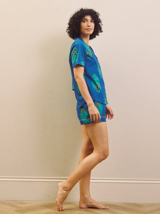 Woman wearing a blue peacock patterned shirt pyjama set against a beige wall.