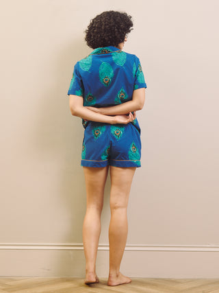 Woman wearing a blue peacock patterned shirt pyjama set against a beige wall.