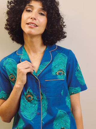 Woman wearing a blue peacock patterned shirt pyjama set against a beige wall.