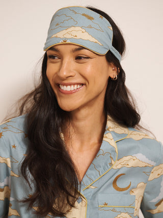Woman wearing a matching eye mask and pyjamas with celestial design on a plain background