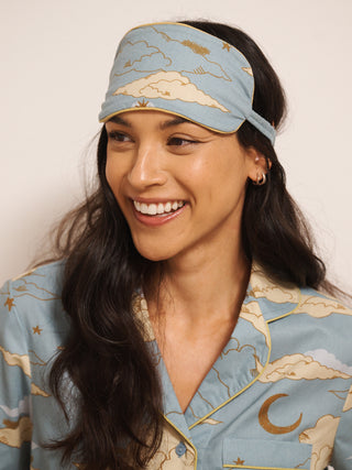 Woman wearing a matching eye mask and pyjamas with celestial design on a plain background