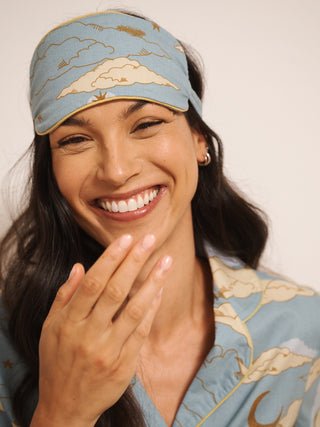 Woman wearing a matching eye mask and pyjamas with celestial design on a plain background